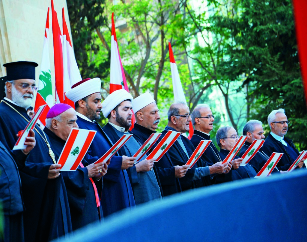 sheikh and priests standing next to each others while holding the a paper with ebanese flag and the lebanese flag all around