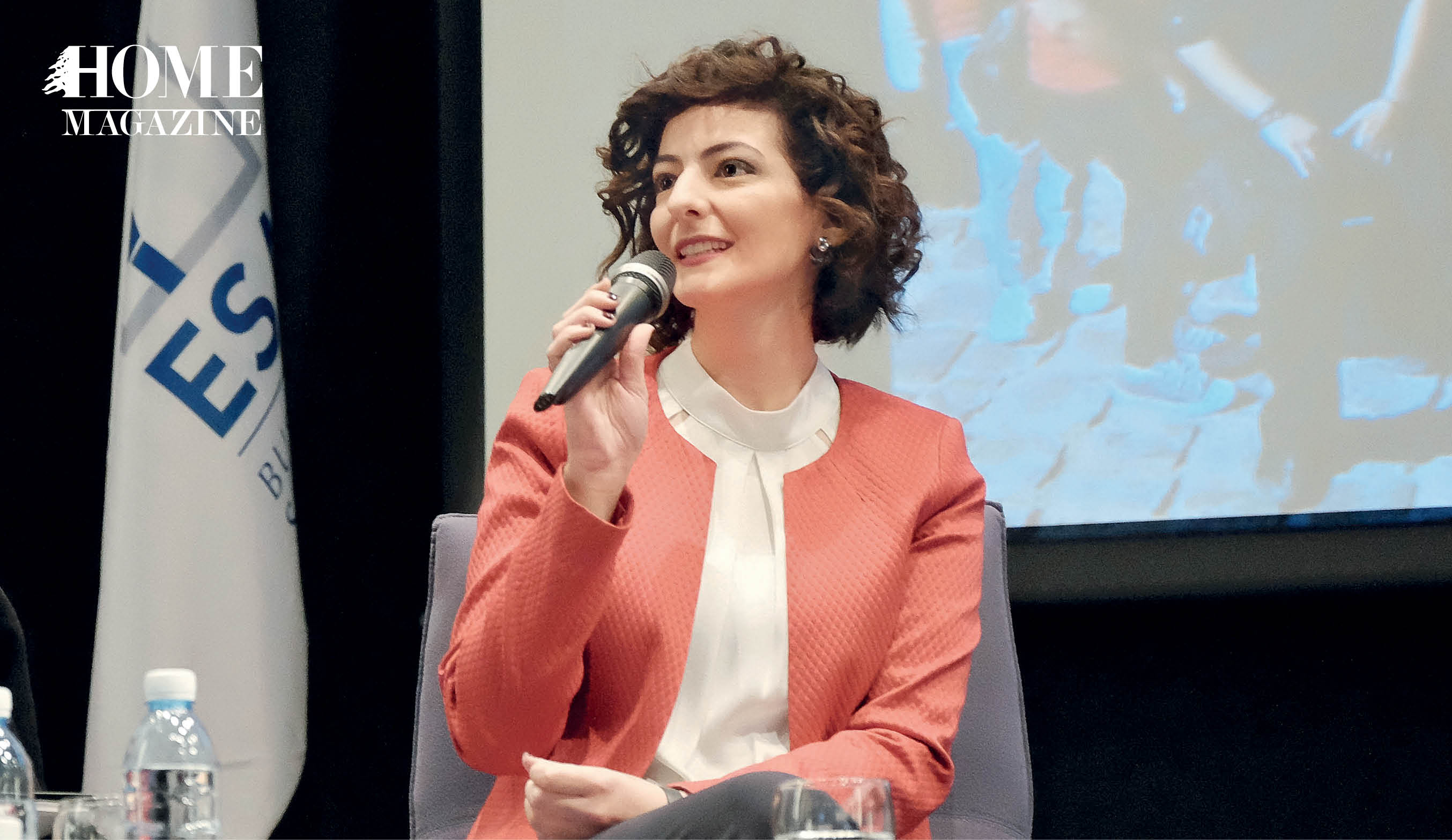 Woman in pink jacket and white blouse speaking on microphone in hand