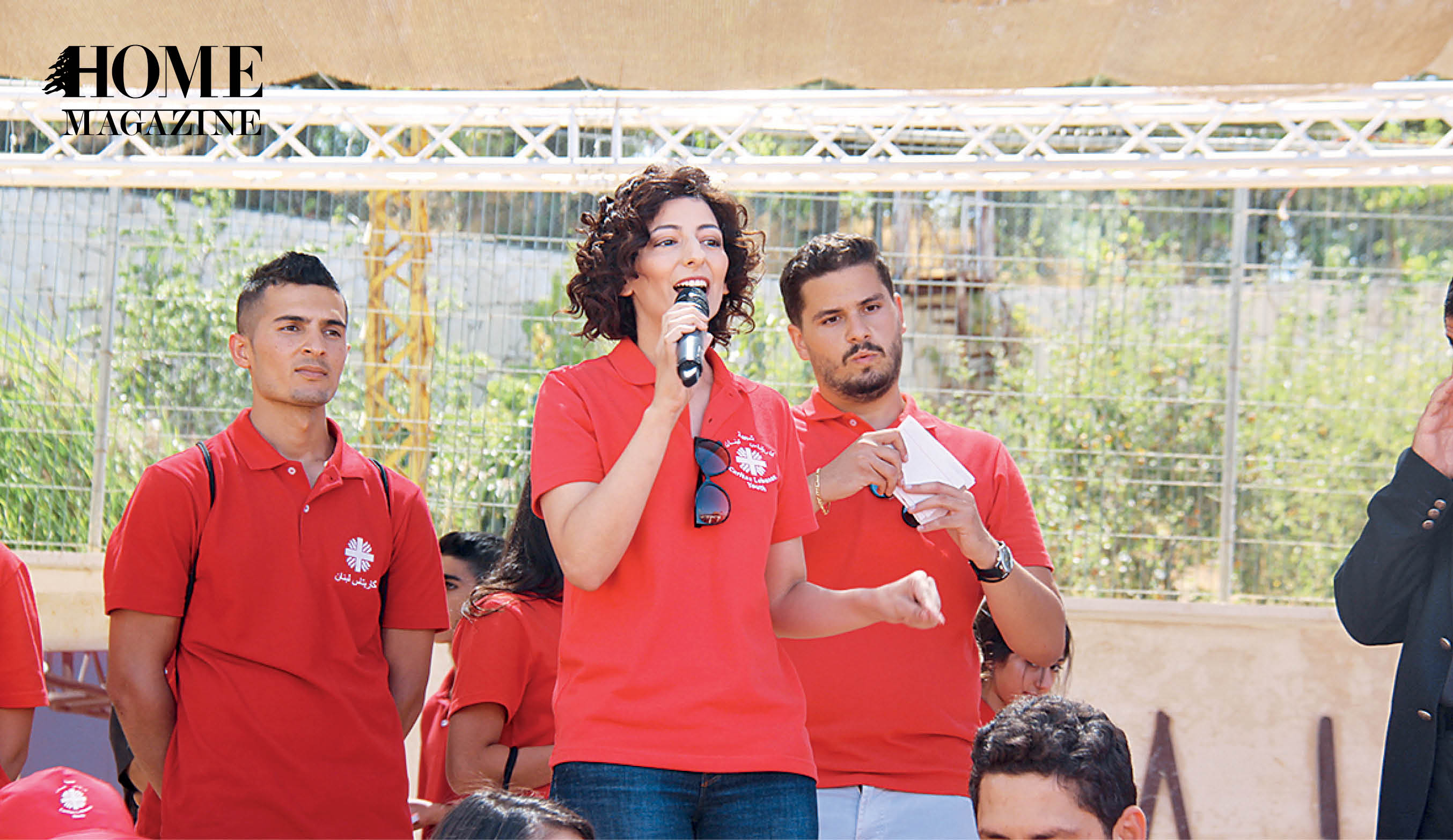 Woman in red tshirt speaking on microphone with two men in red tshirts behind