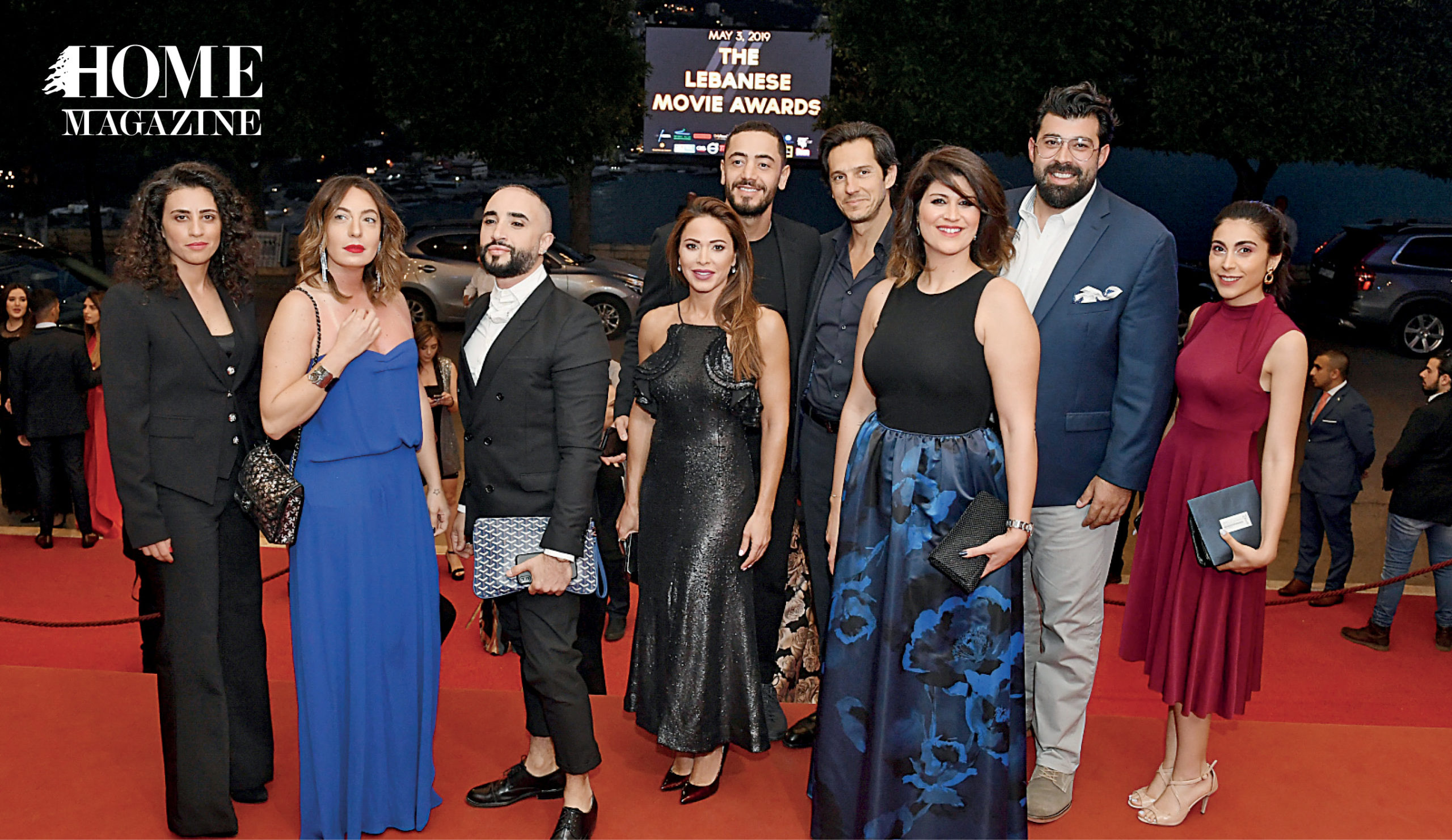 Group of men and women on red carpet in evening dresses and suits